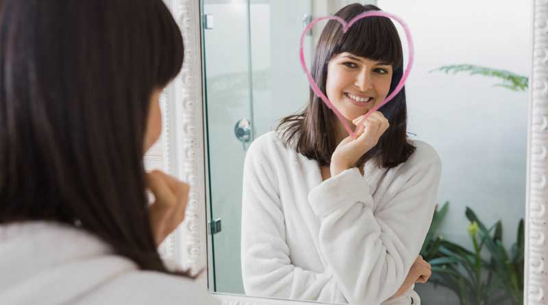 Young woman looking in the mirror at a heart shape drawn around her face
