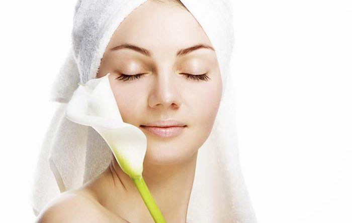 Woman wearing a towel over her hair placing a flower against her facial skin
