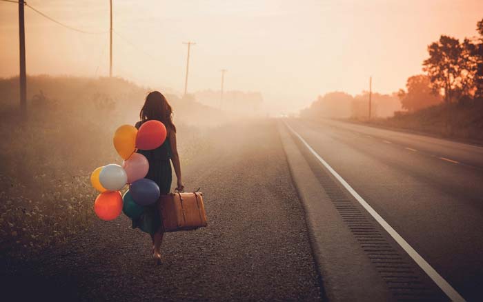 Girl carrying balloons and walking down a long road