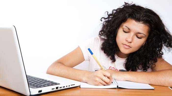 Girl writing in notebook near laptop