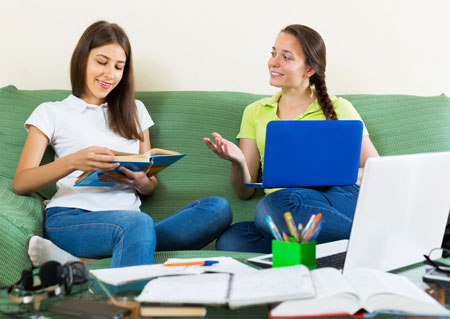 Teenage girls studying together with books and laptops