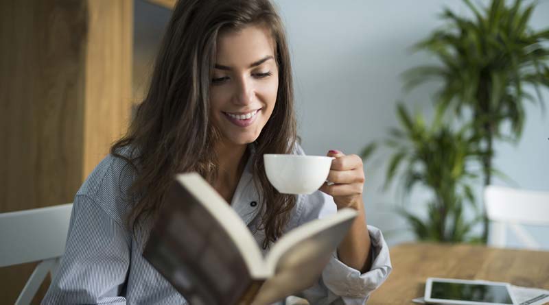 Young woman reading a book while drinking coffee