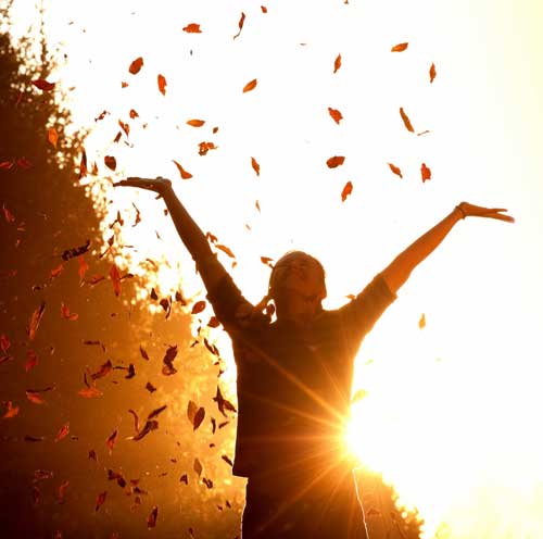 Girl throwing leaves into the air at sunset