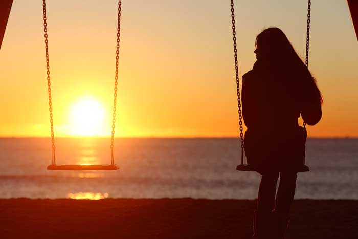 Girl sitting on a swing at sunset with an empty swing beside her