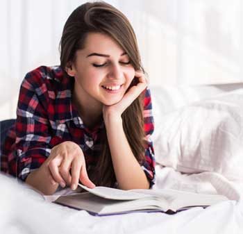 Girl lying on a bed reading a book and smiling