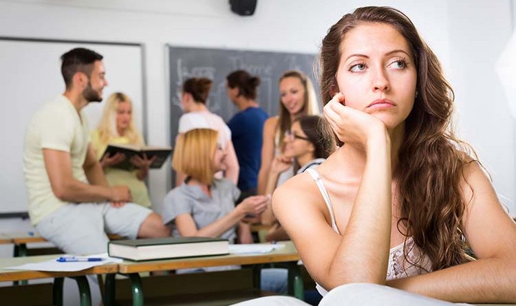 Female student sitting alone in class thinking with other students talking in the background