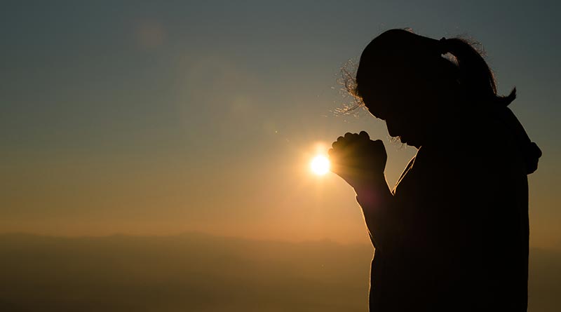 Young woman praying at sunset
