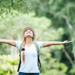 Young happy woman with arms raised in gratitude enjoying nature