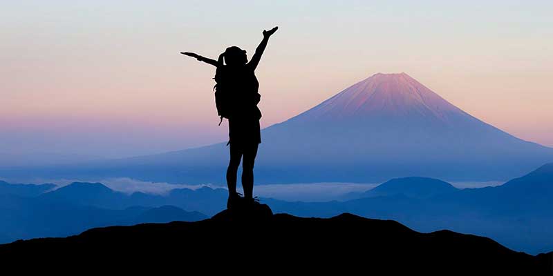 Young girl raising her hands up while standing on a mountain top