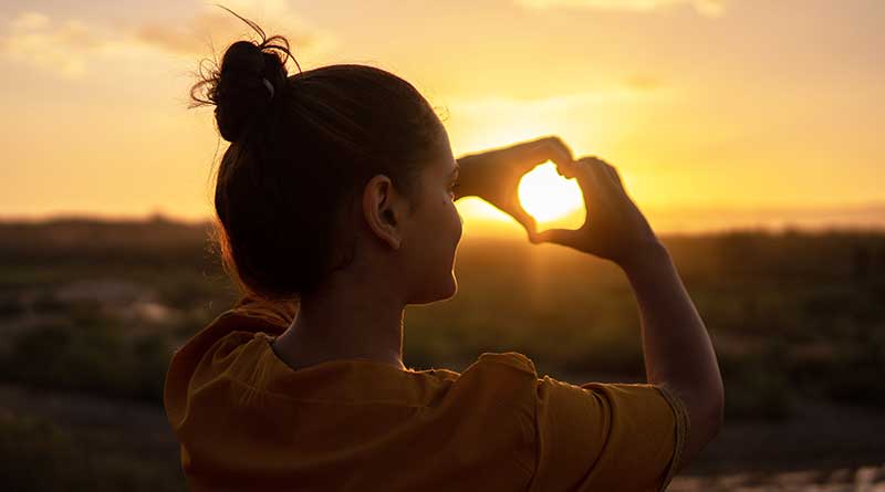 Young woman forming a heart sign with her hands at sunset