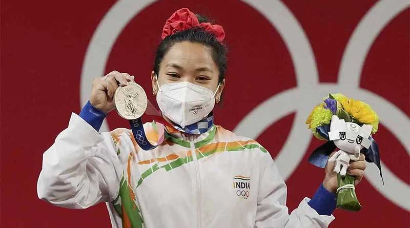 Mirabai Chanu holding up her Olympic silver medal for weightlifting