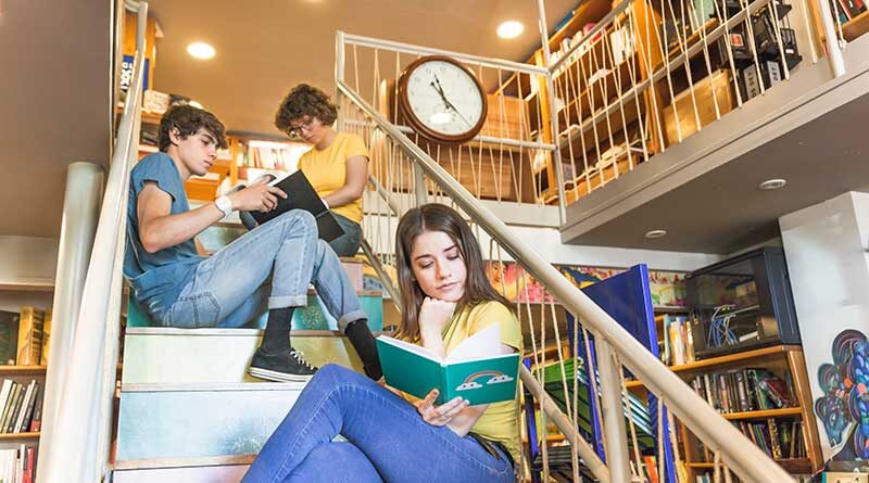Teens reading while sitting on steps inside a library