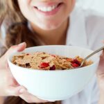 Young woman eating her breakfast of cereal with milk and strawberries