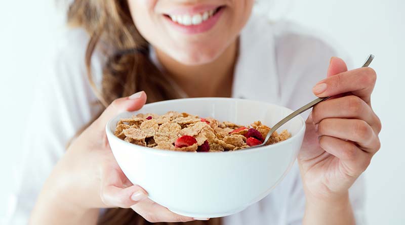 Young woman eating her breakfast of cereal with milk and strawberries