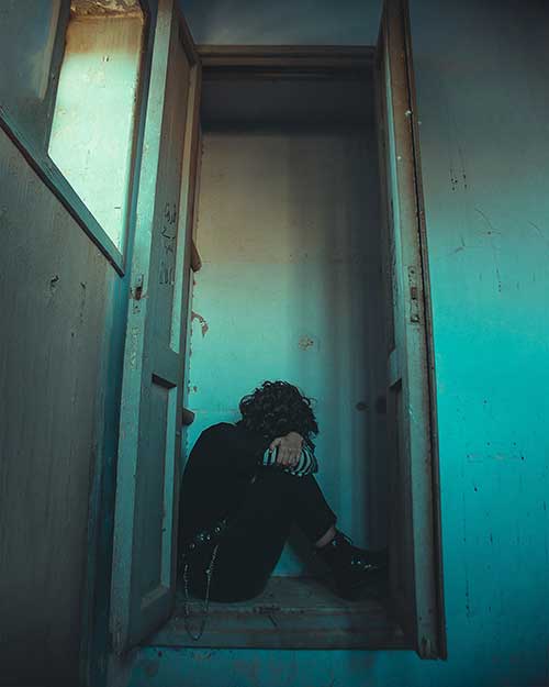 Depressed young woman sitting in the doorway of a room