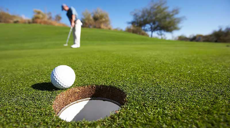 Golf player hitting a golf ball towards a hole.