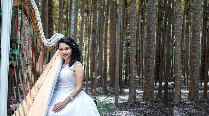 Meagan Pandian in a white dress holding a harp